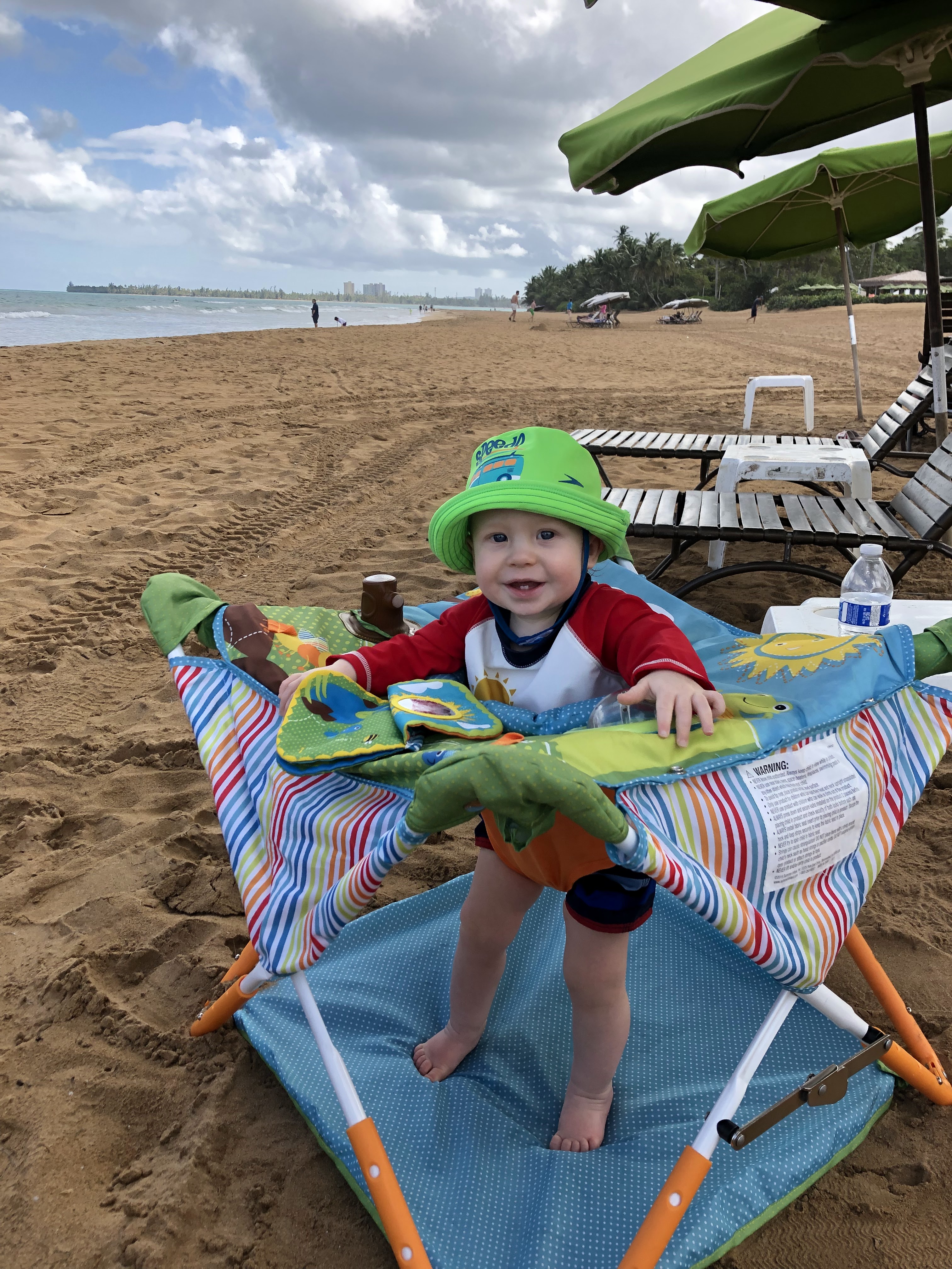 Smiling infant in a collapsible stand-up jumper on a beach in Puerto Rico