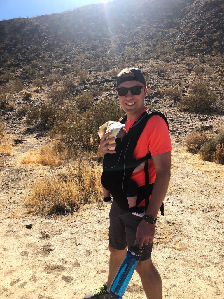 Man wears young infant in baby carrier while hiking