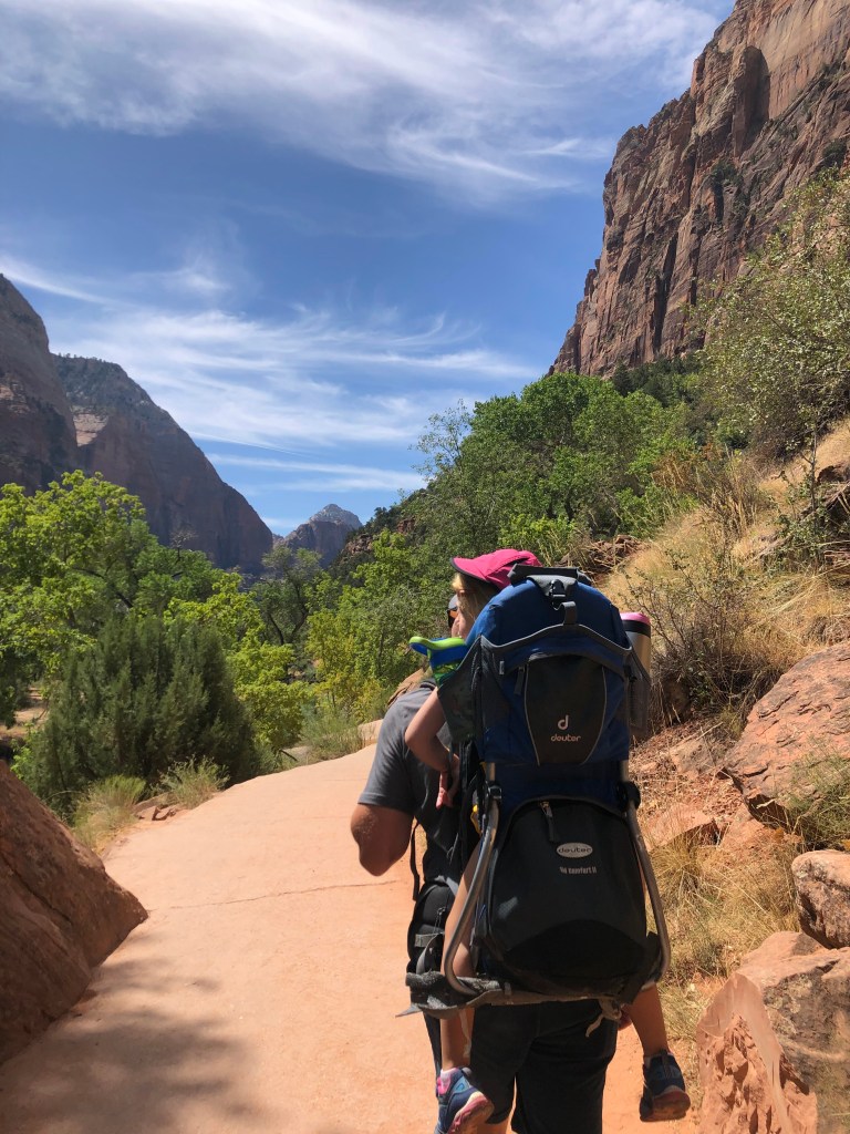 Man hiking on a path through mountains with a 3-year-old child on his back in a hiking backpack